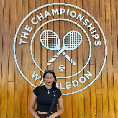 Halimah Kyrgios is standing in front of the giant Wimbledon logo in the picture.